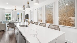 Une cuisine moderne dotée d’un îlot en marbre, de luminaires suspendus et d’un coin repas avec des chaises en osier.
