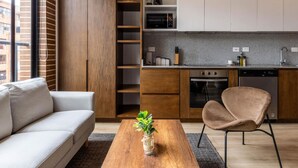 Un appartement moderne comprenant un canapé, une table basse en bois, un fauteuil, une cuisine avec des meubles blancs, un four à micro-ondes et un lave-vaisselle.