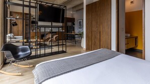 Une chambre d’hôtel moderne dotée d’un grand lit, d’un coin salon avec des fauteuils, d’une télévision et d’une armoire en bois.
