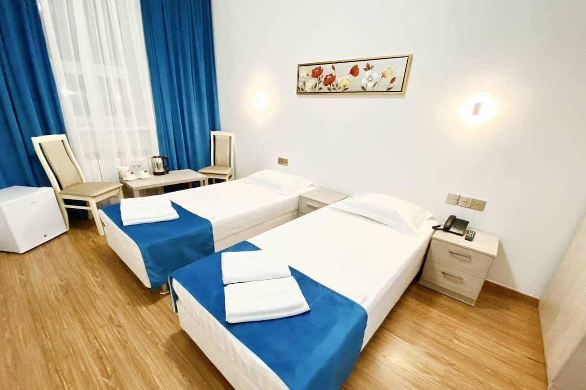 Habitación de hotel con dos camas, un escritorio, una silla, una mesita pequeña, una mesita de noche y teléfono en la pared.