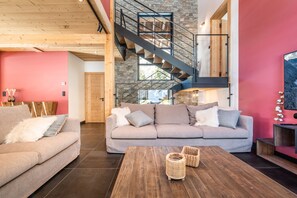 A modern living room with a grey sofa, a wooden coffee table, and a staircase with a glass railing. - AZOBE - Large Chalet with Hot Tub and Sauna (Montriond)