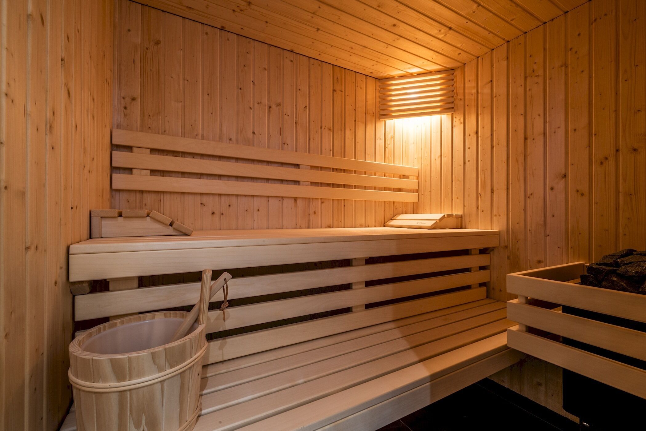 A wooden sauna with benches and a bench seat, a wooden wall, and a light fixture.