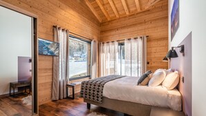 Ein Schlafzimmer mit Holzboden, einem Bett mit weißer Bettwäsche, einem großen Fenster mit Vorhängen und einem Gemälde an der Wand.