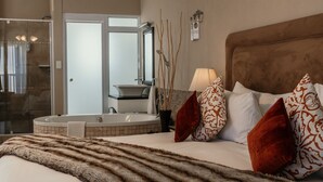 A bedroom with a large bed, a headboard, a bedside table, a lamp, and a view of a bathroom with a bathtub and a mirror.