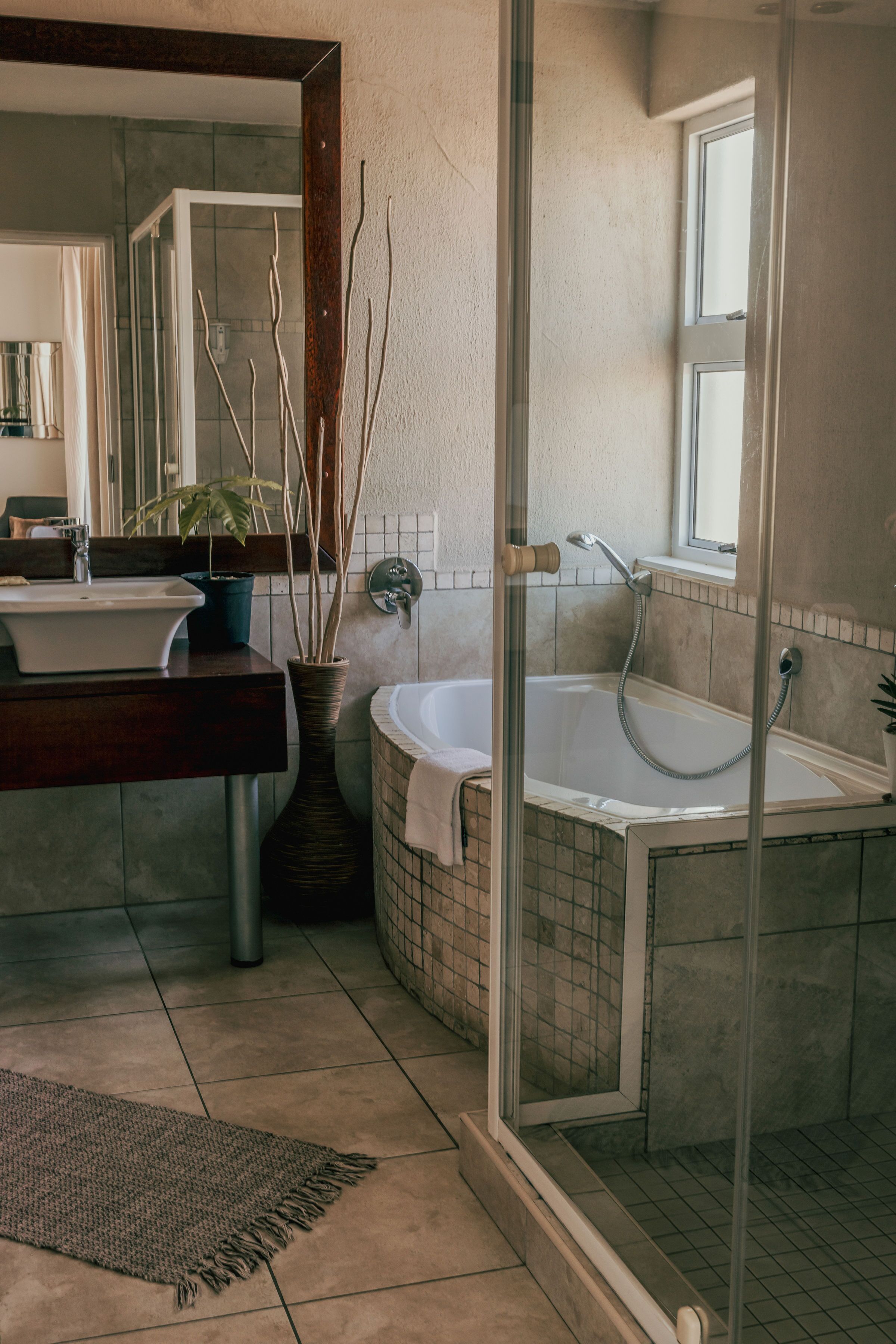 A bathroom with a glass-enclosed shower, a bathtub, a sink, and a potted plant.