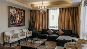 A living room with a black sofa, two patterned armchairs, a wooden coffee table, and a chandelier.