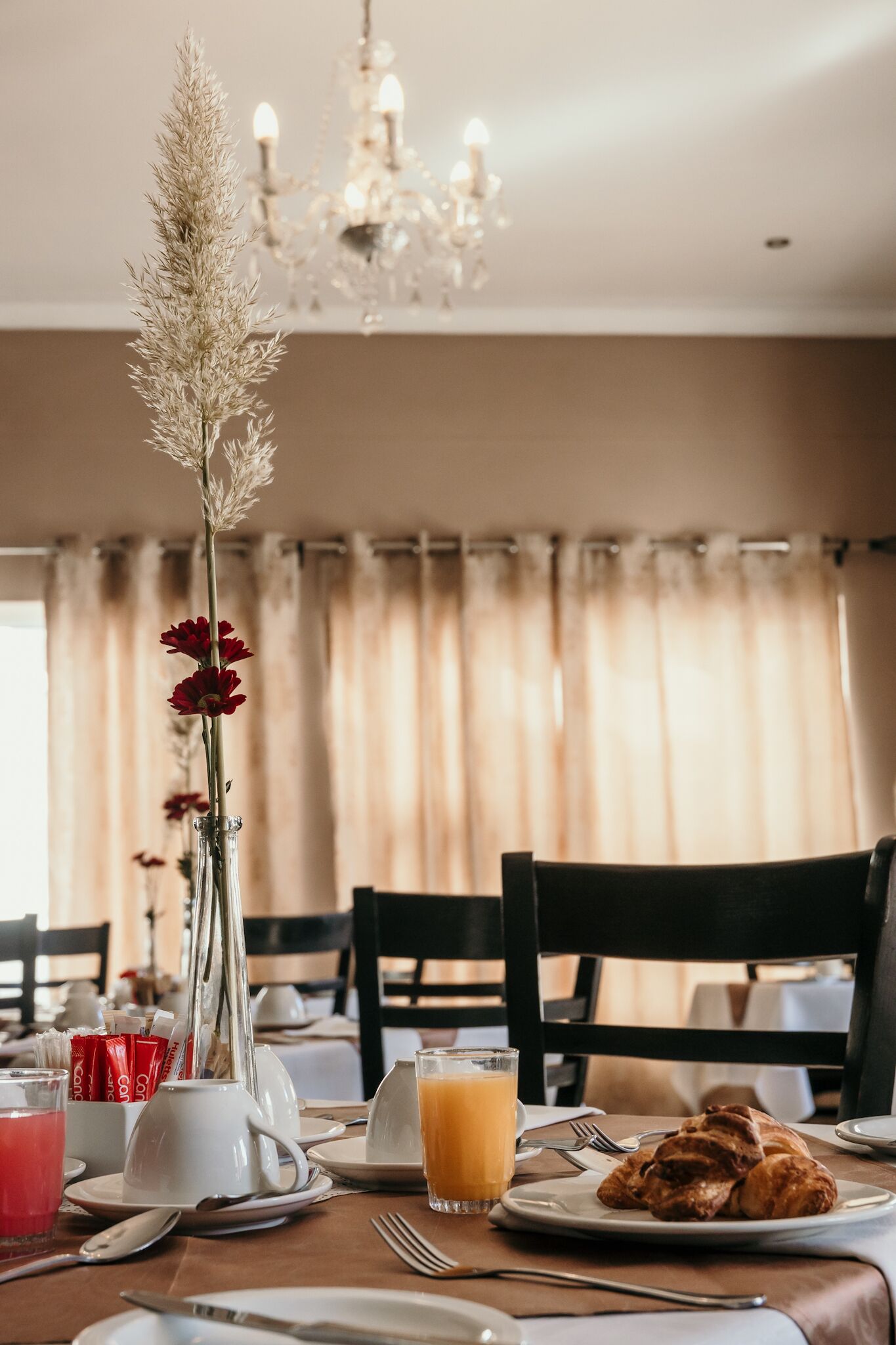 Ein Esstisch mit Frühstücksgebäck, eine Vase mit Blumen und eine Chandelier im Hintergrund.