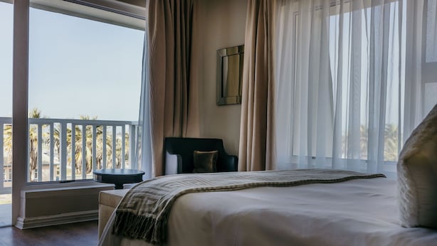 A bedroom with a large bed, a nightstand, a chair, and a window with curtains.