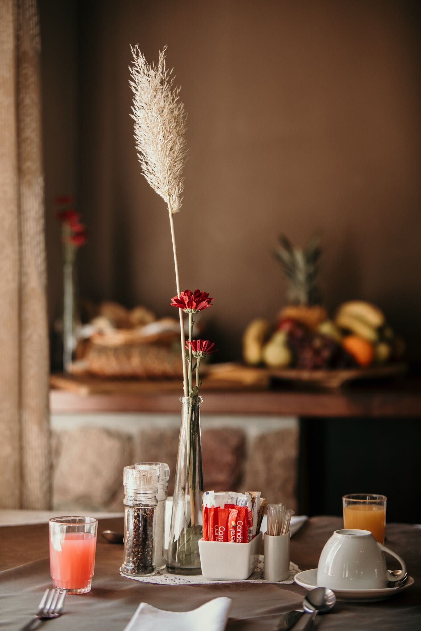 Ein Frühstückstisch mit Obstschale, einer Vase mit Trockenblumen und einem Glas Orangensaft.
