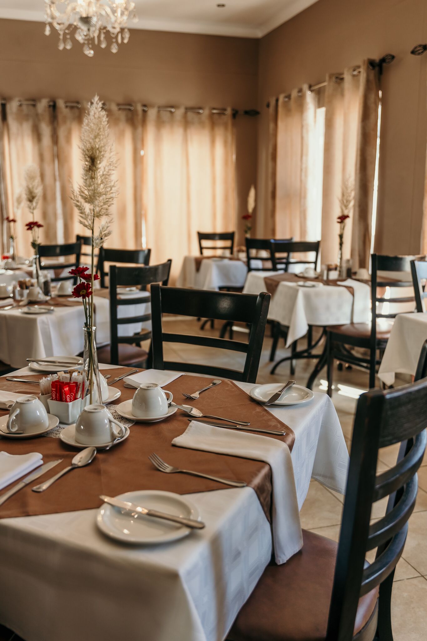 Un restaurante con mesas dispuestas para comer, con manteles blancos y sillas marrones.