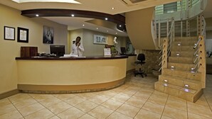 A reception area with a curved counter, framed certificates, and a staircase with metal railings.