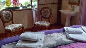 Quarto com cama, duas cadeiras, janela, pia e espelho.