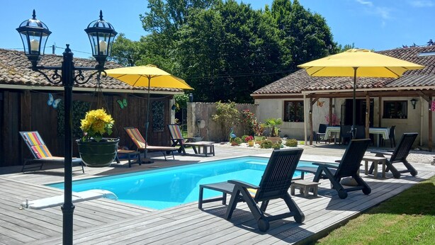 Um deck de madeira com piscina, cadeiras de descanso e dois guarda-sóis amarelos.