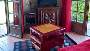 Quarto com teto de madeira, televisão sobre um armário de madeira, sofá vermelho e tapete estampado.