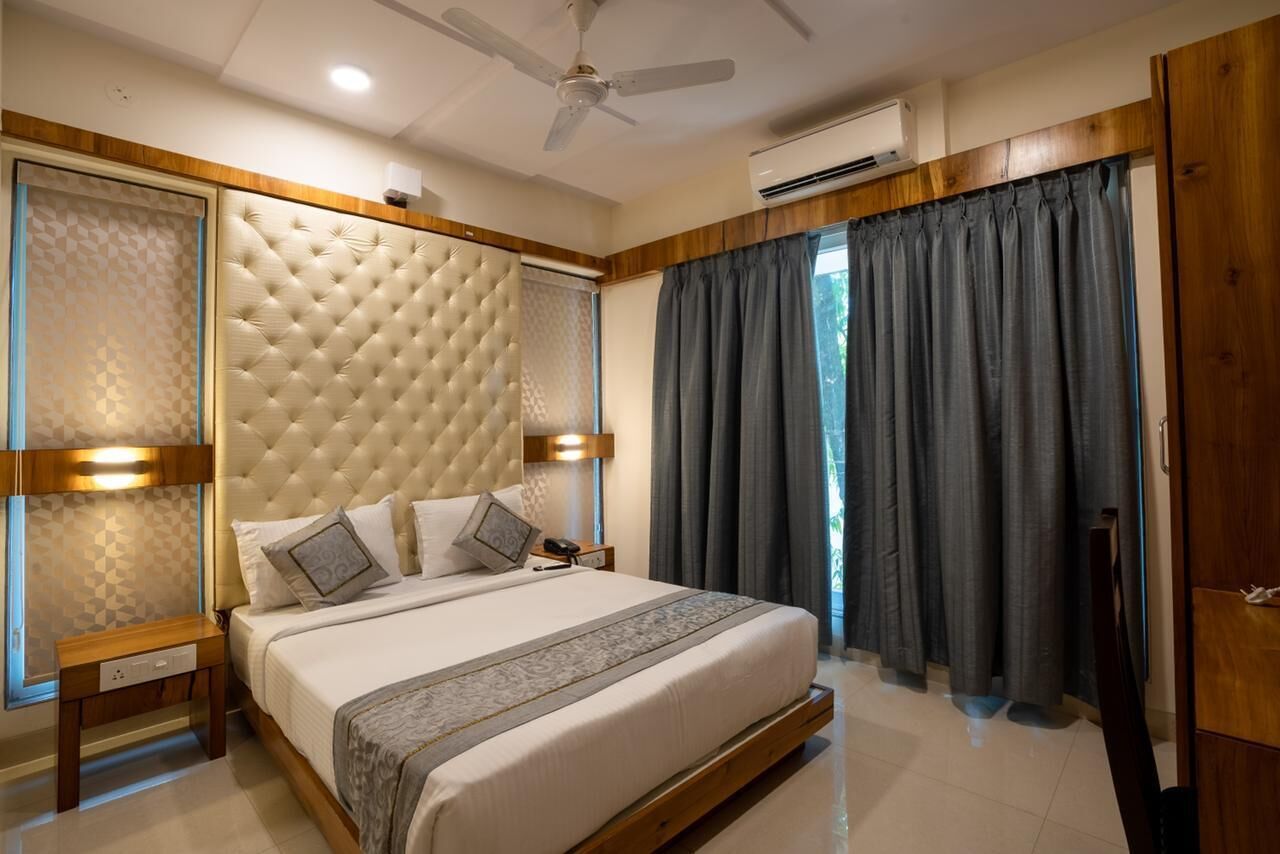 A bedroom with a tufted headboard, a bed with pillows, a nightstand, a ceiling fan, and a window with curtains.