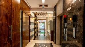 Un hall d’hôtel moderne doté d’une porte en bois, d’une porte en verre, d’un sol en marbre et d’un espace de réception avec un téléphone et un ascenseur.