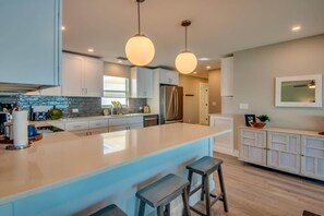 Una cocina moderna con una isla grande, iluminación colgante y un refrigerador empotrado.
