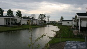 Une rangée de maisons mobiles blanches, avec un petit étang au premier plan.