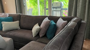 Un canapé modulable avec plusieurs coussins, une fenêtre avec des rideaux et une vue sur la verdure à l’extérieur.