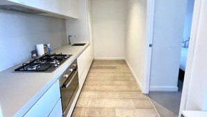 A narrow kitchen with a gas stove, cabinets, and a wooden floor.