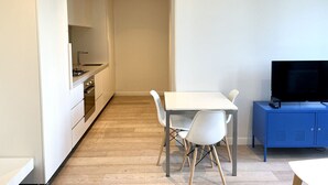 A compact kitchen with modern appliances, a dining area with a table and chairs, and a television on a blue cabinet.