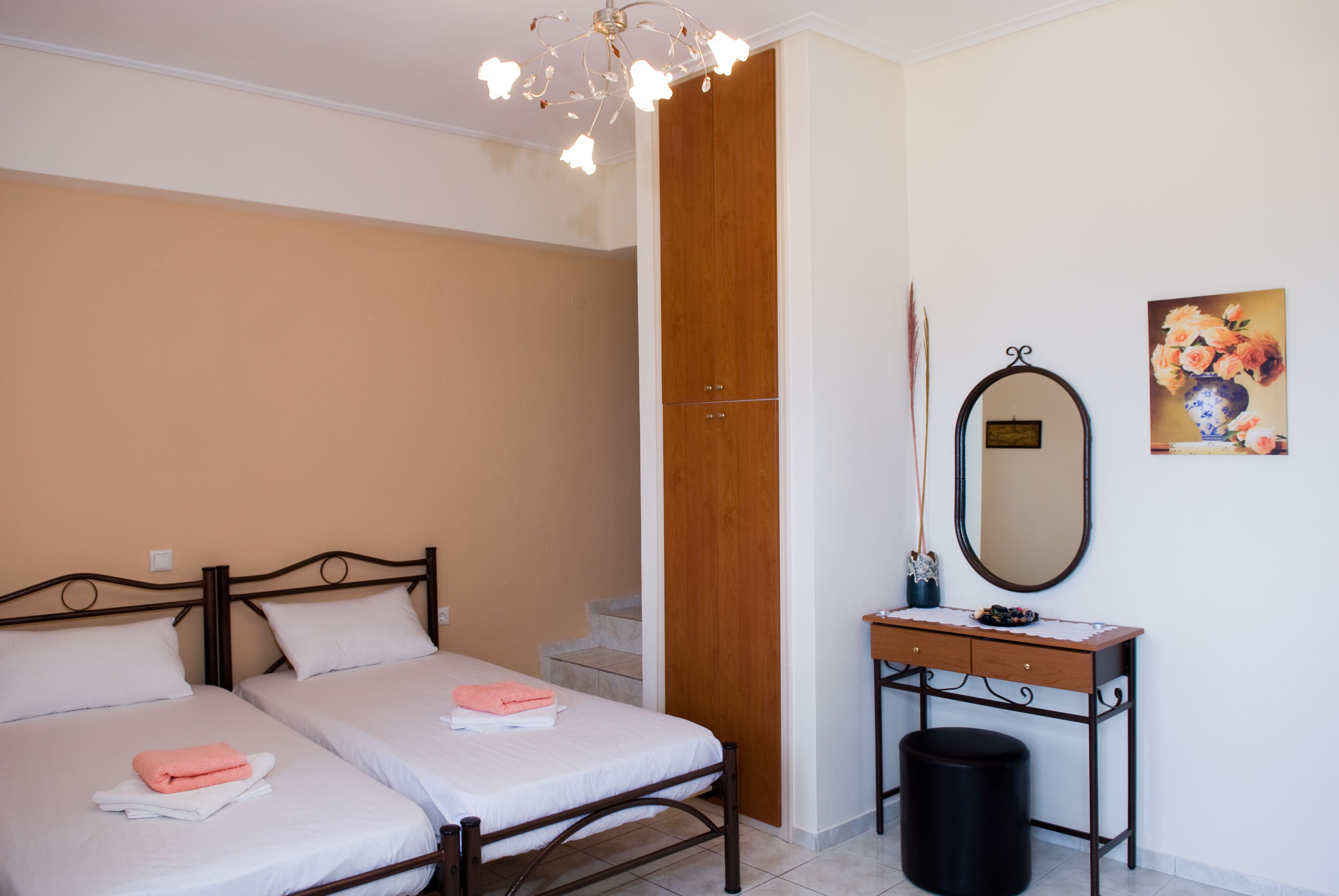 A bedroom with two beds, a wooden wardrobe, a mirror, and a small table with a vase.