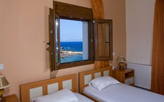 Un dormitorio con dos camas, una ventana con vista al mar, una mesita de noche y una lámpara.