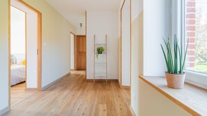 A hallway with wooden flooring, a plant on a shelf, and a window with a view. - Gîte un Air de Campagne (Gergny)