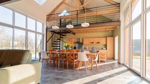 A spacious living area with a high ceiling, a dining table surrounded by chairs, and a staircase leading to an upper level. - Gîte un Air de Campagne (Gergny)