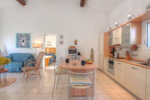 Eine moderne Küche mit einer zentralen Kochinsel, ein Essbereich mit Stühlen und ein Wohnzimmer mit Sofa und Couchtisch.