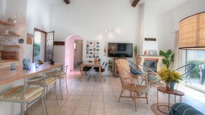A spacious living area with a dining table, chairs, a TV, and a fireplace. - Kazamasavani - Belle maison proche mer ! (Cervione)