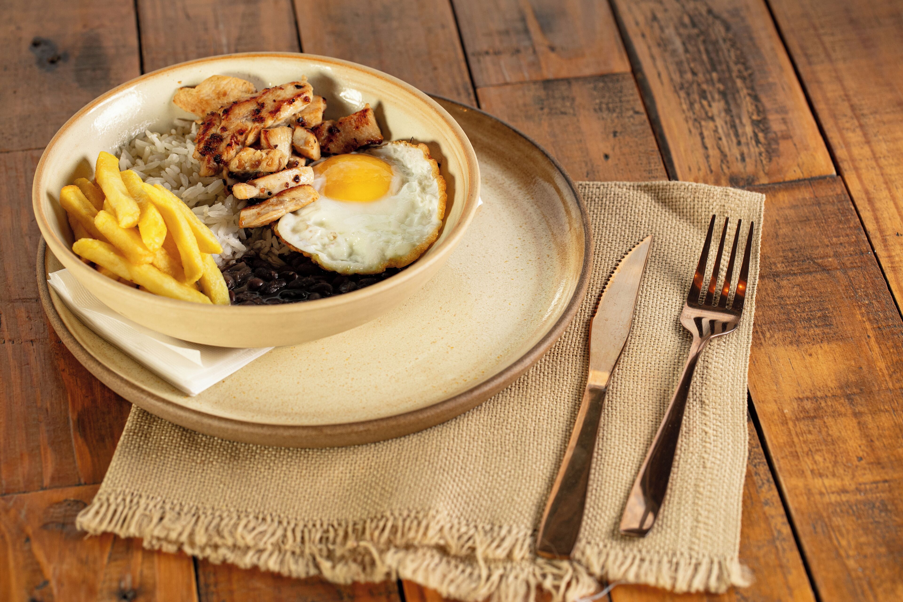 Ein Teller Essen mit Reis, schwarzen Bohnen, Spiegelei und Hähnchen auf einem Holztisch.