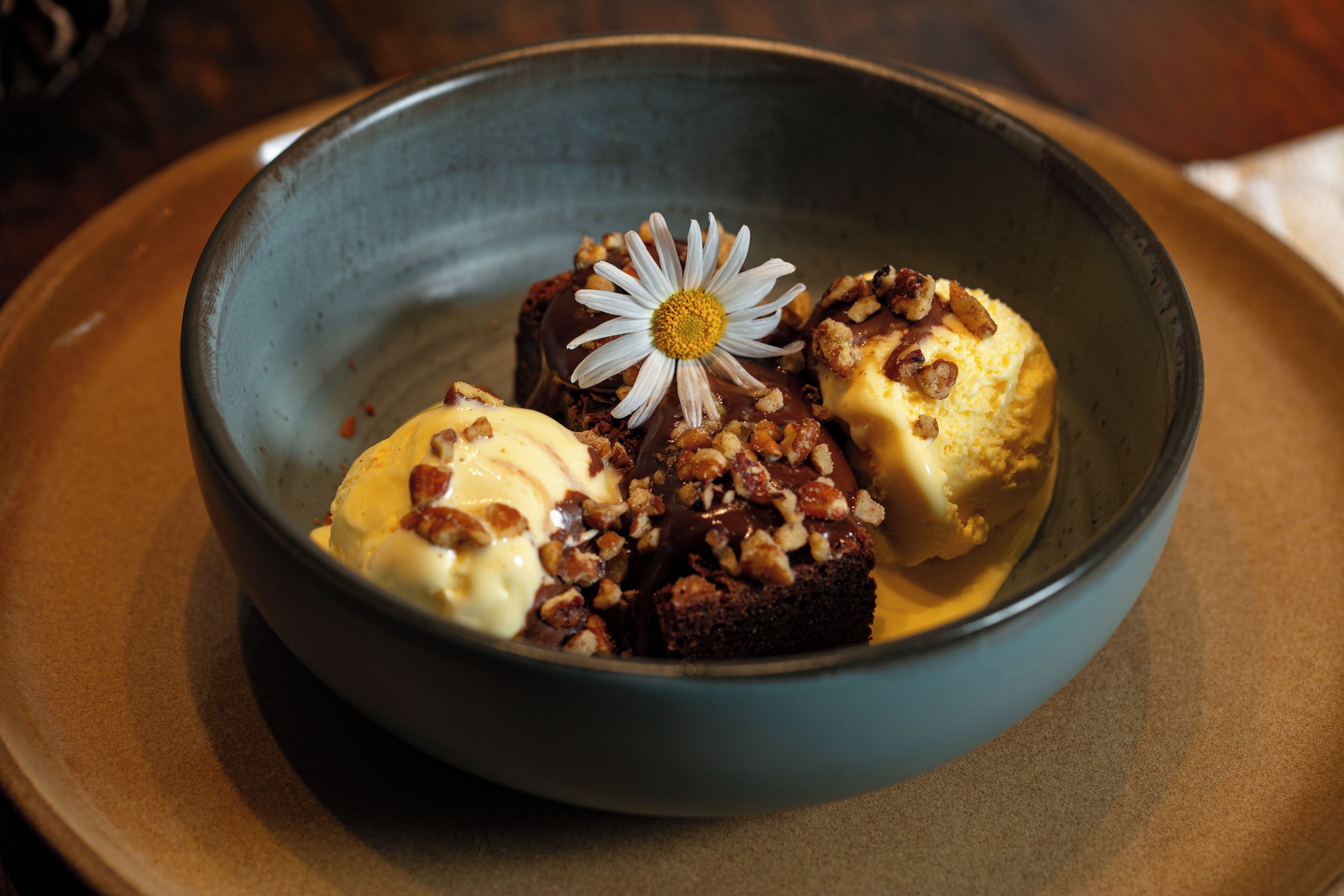 A bowl of dessert with ice cream and a cake topped with nuts and a flower.