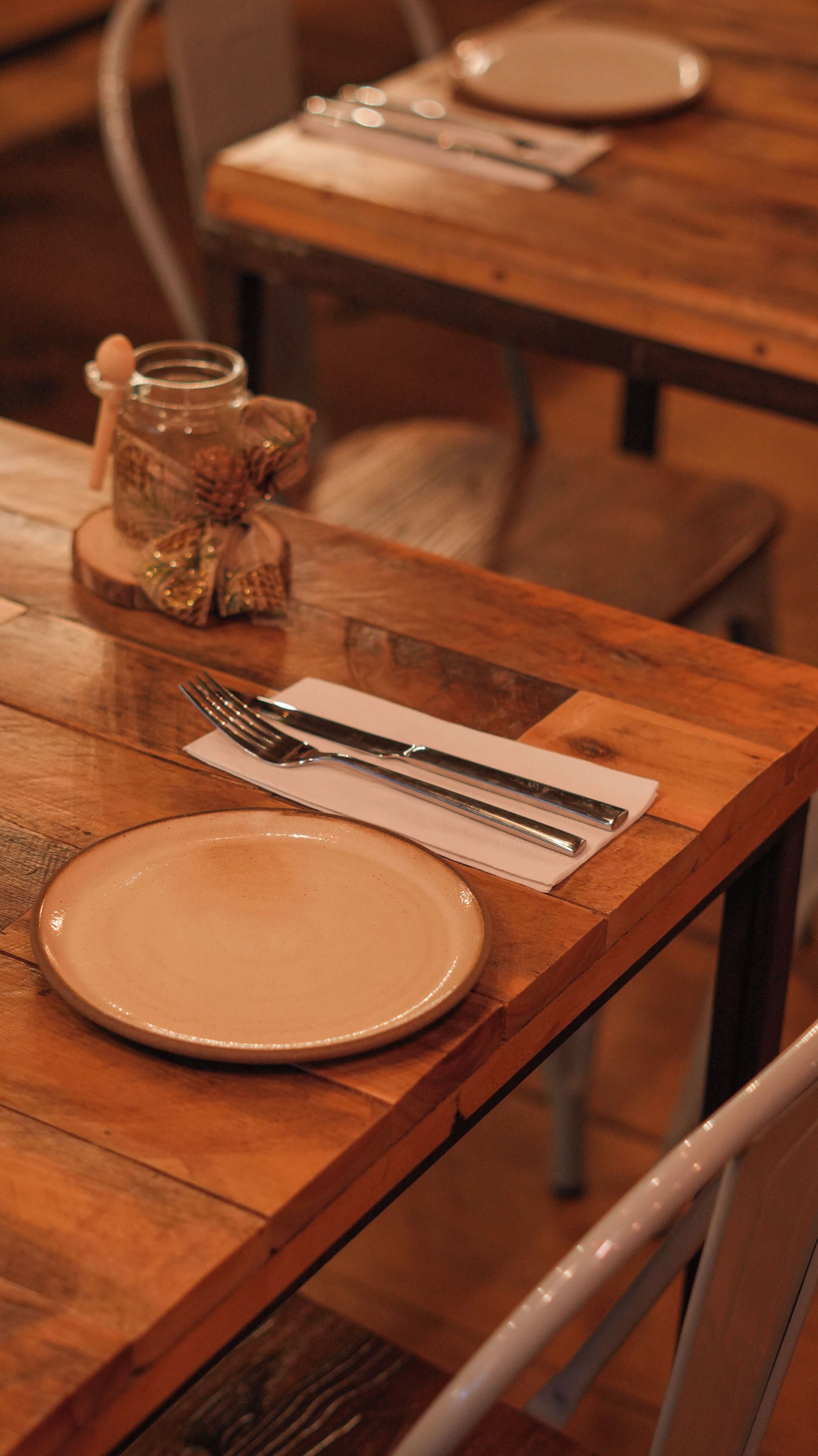 A wooden dining table with a plate, fork, and knife set on a napkin.