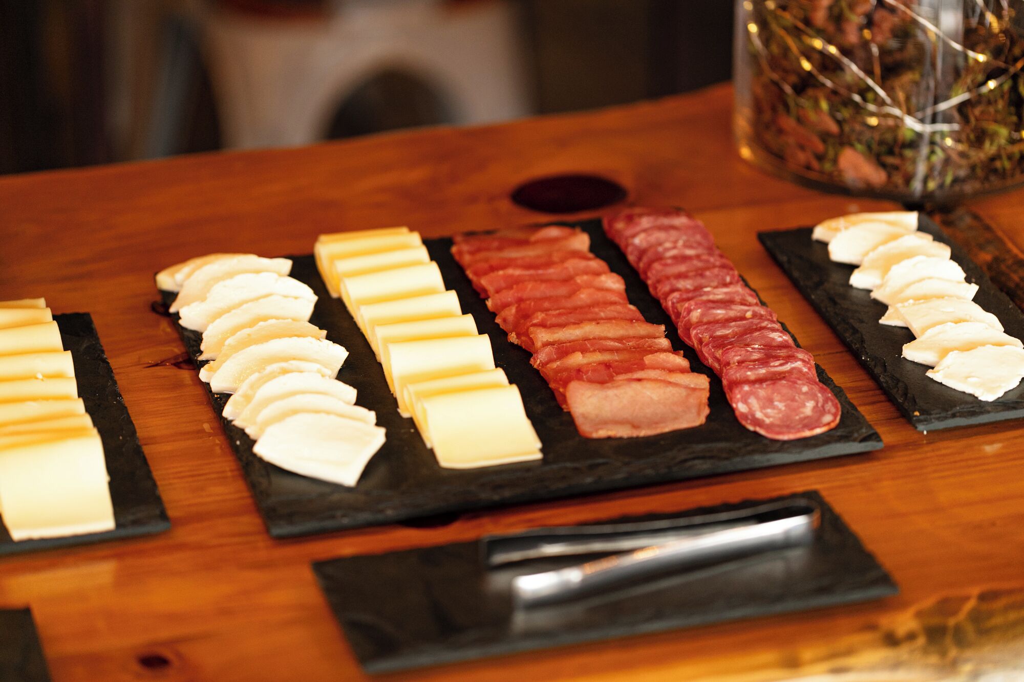 A wooden table with a variety of sliced meats and cheeses arranged on slate boards.