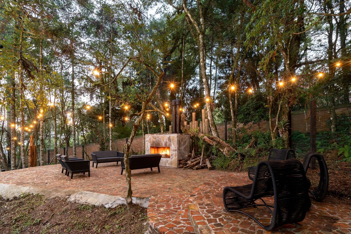 A patio with a stone fireplace, outdoor seating, and string lights in a wooded area.