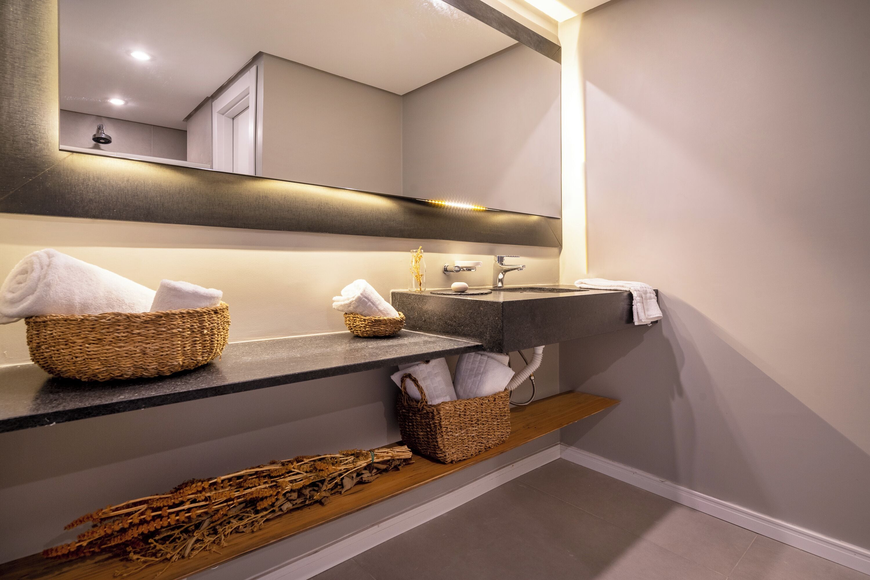 Un baño con un espejo grande, un lavabo y dos cestas de mimbre en la encimera.