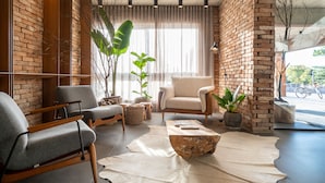 A modern living room with a brick wall, two grey armchairs, a beige sofa, a wooden coffee table, and a large window with sheer curtains. - Jangal das Araucárias Swan Design Hotel Canela (Canela)