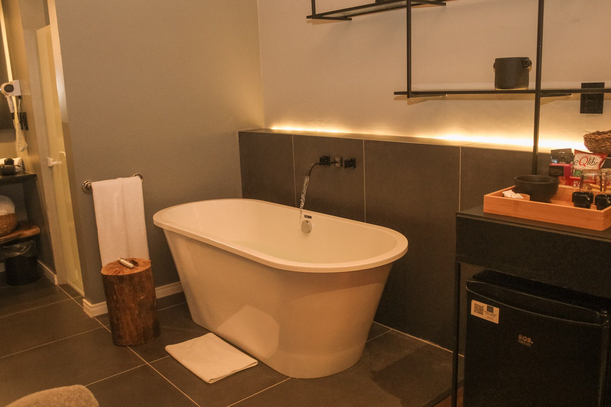 A modern bathroom with a freestanding bathtub, a towel rack, and a shelf with toiletries.