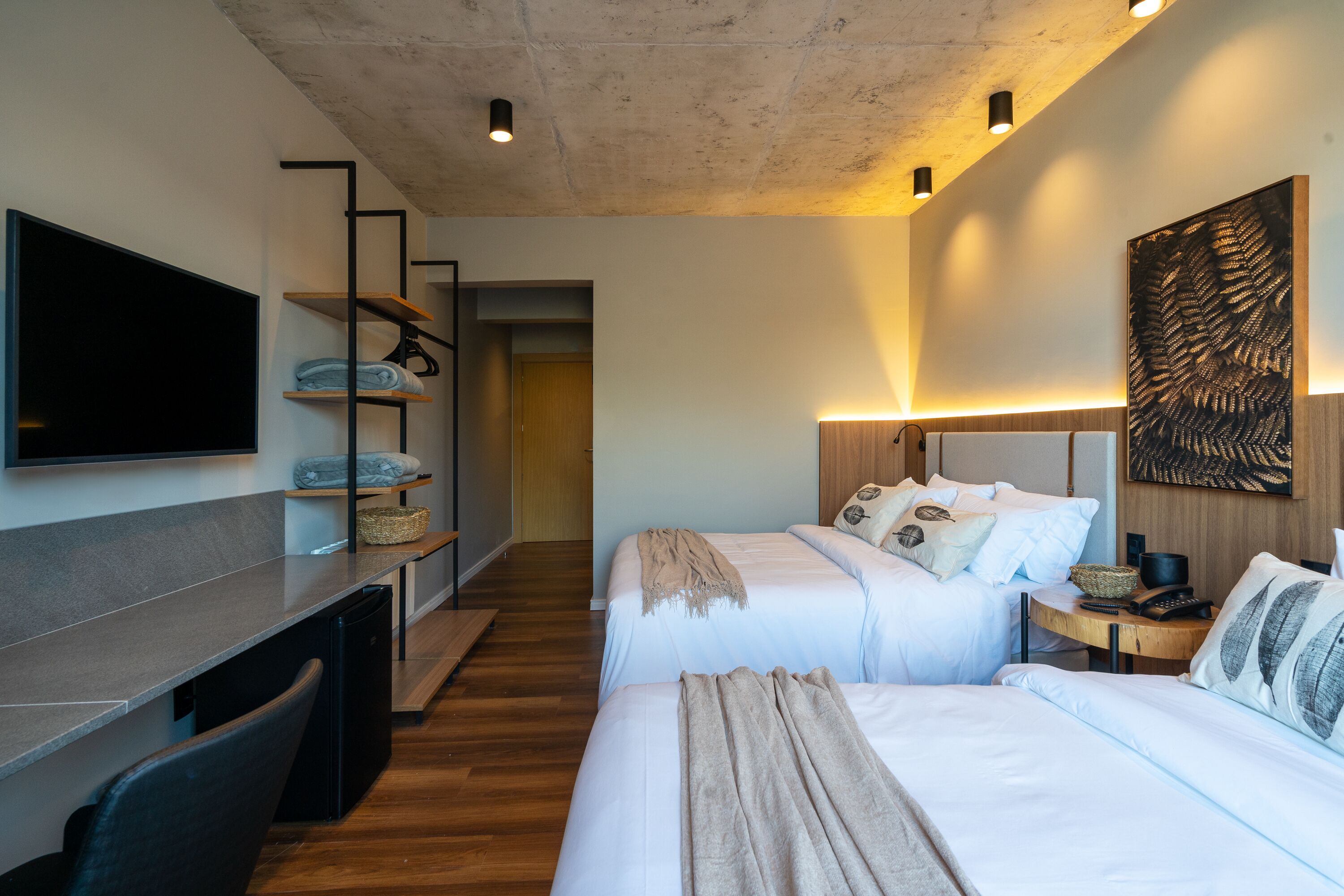 Une chambre d’hôtel moderne équipée de deux lits, d’un téléviseur à écran plat, d’un bureau et d’une grande œuvre d’art abstraite accrochée au mur.