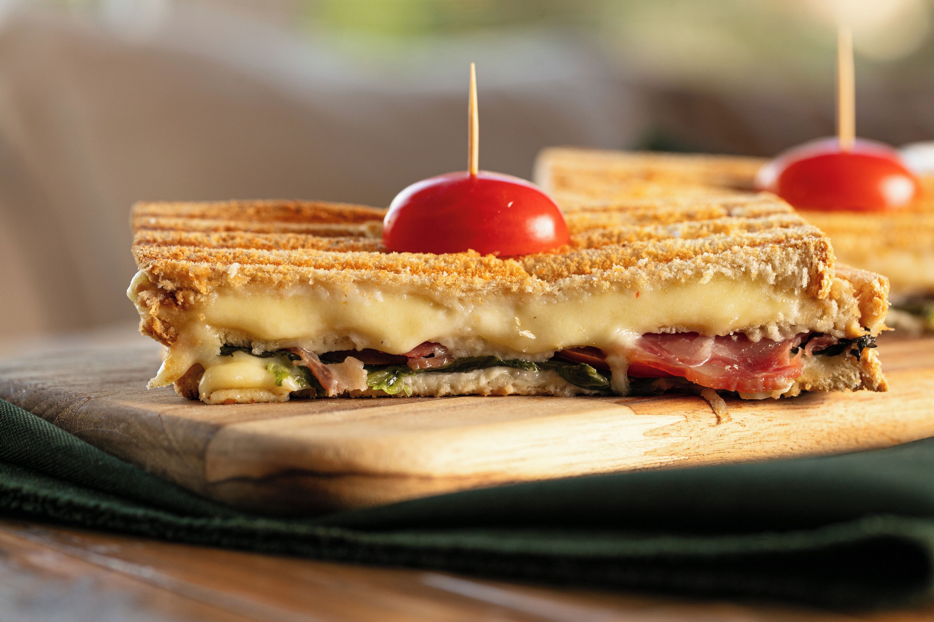 A sandwich with a cherry on top, placed on a wooden board.