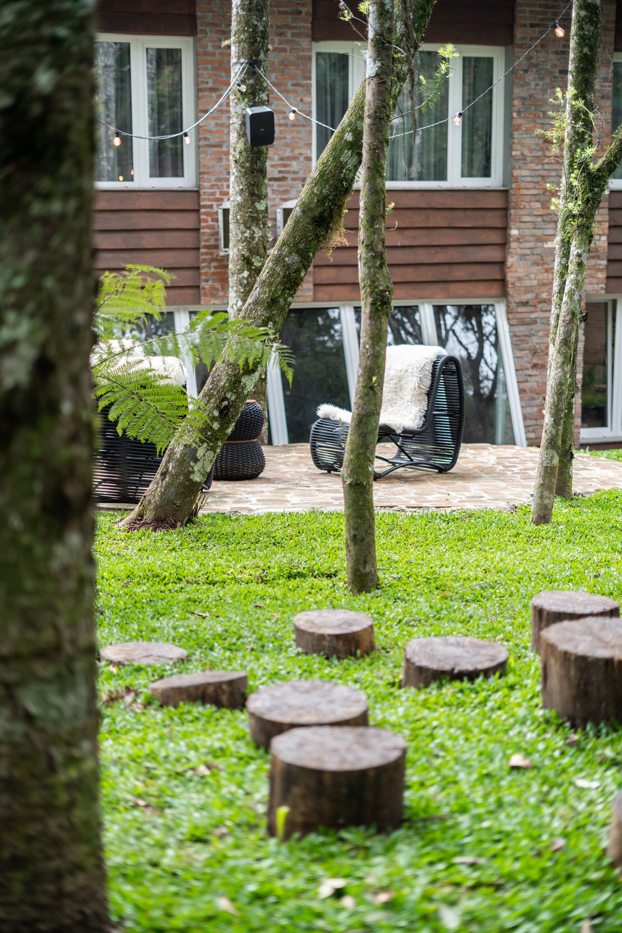 Een tuin met bomen, een houten bankje en een bakstenen gebouw op de achtergrond.