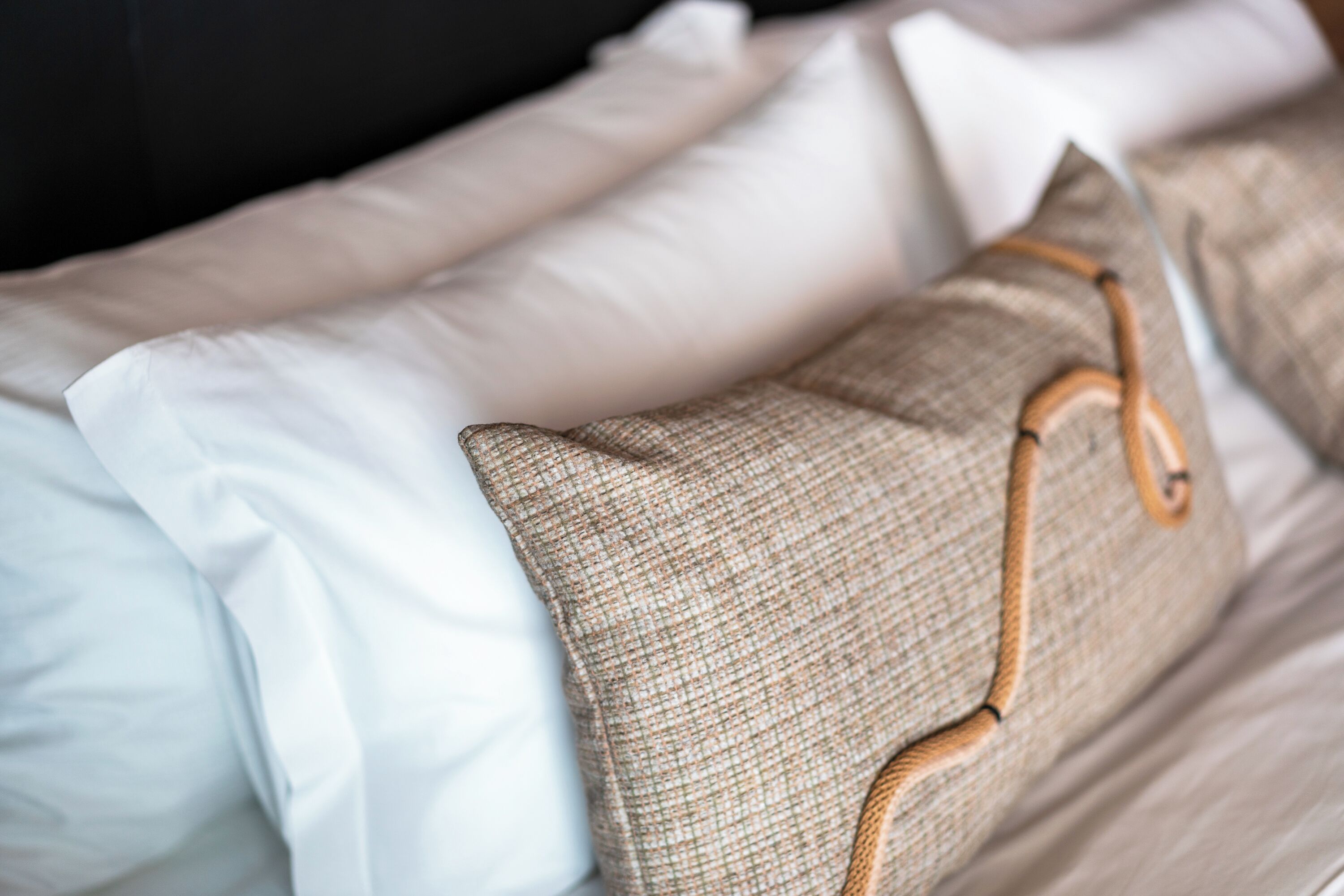 A bed with white and beige pillows, a brown woven pillow, and a wooden headboard.