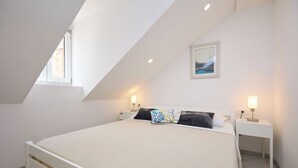 A bedroom with a bed, two bedside tables, a nightstand, a window, and a picture on the wall.