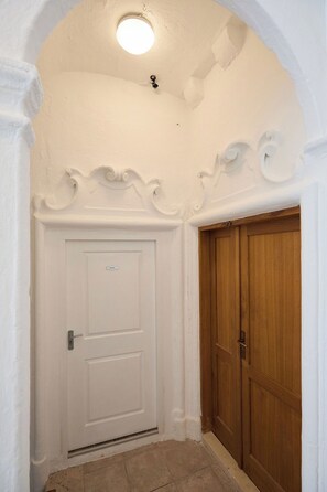 Una porta bianca con un'angusta finestra sopra, una porta di legno adiacente e un soffitto decorato.
