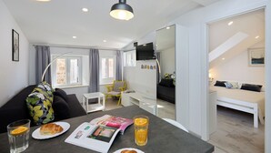 A modern living room with a sofa, a dining table with a magazine, and a breakfast setup with croissants and orange juice.