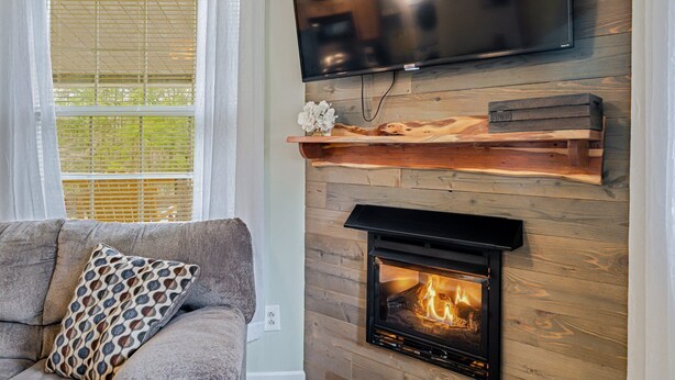 A living room with a fireplace, a mounted TV, and a window with blinds. - Cabin w/ Hot Tub on Small Pond (Rockwood)