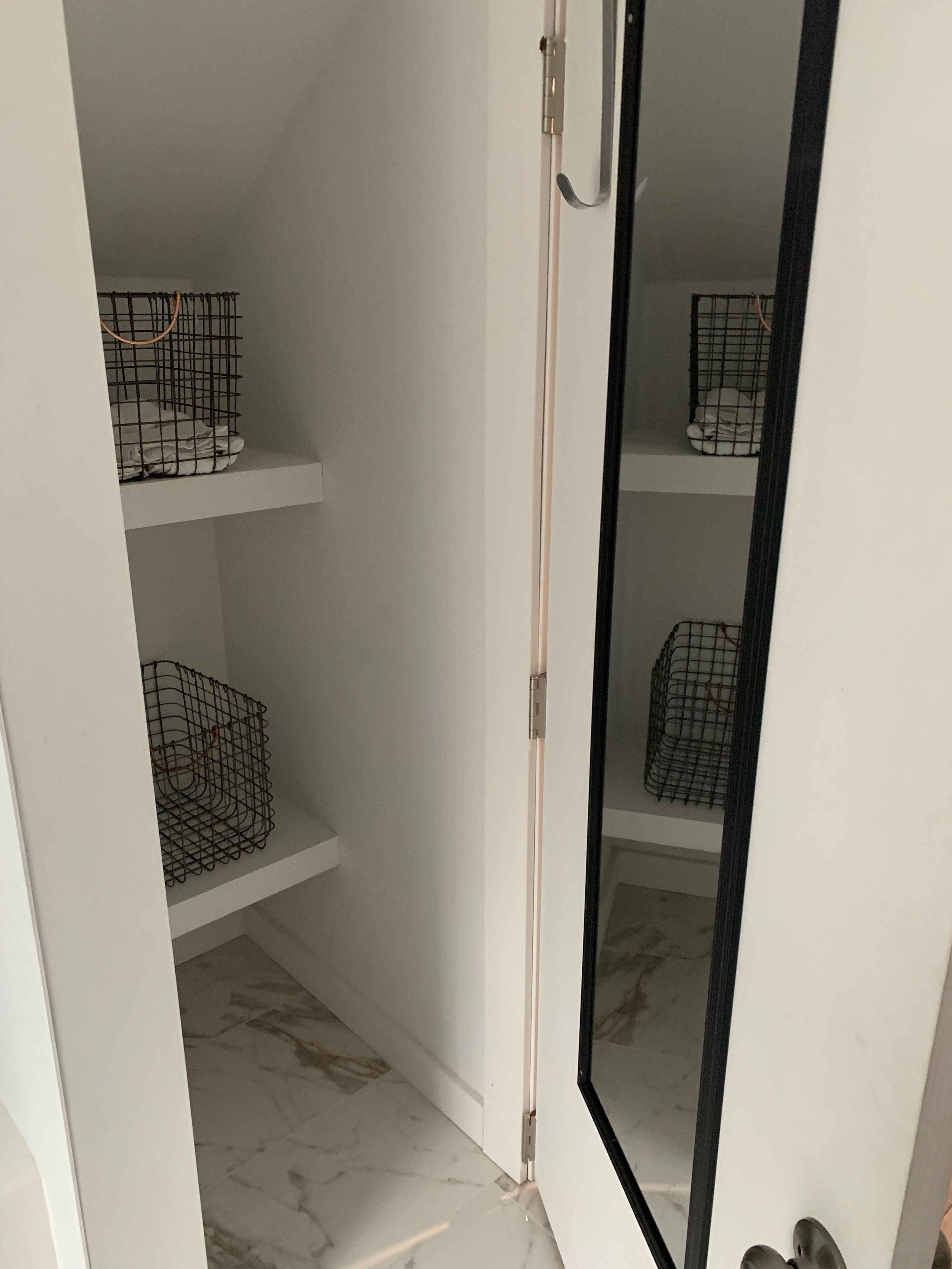 A room with a white door, a marble floor, and two wire baskets on shelves.