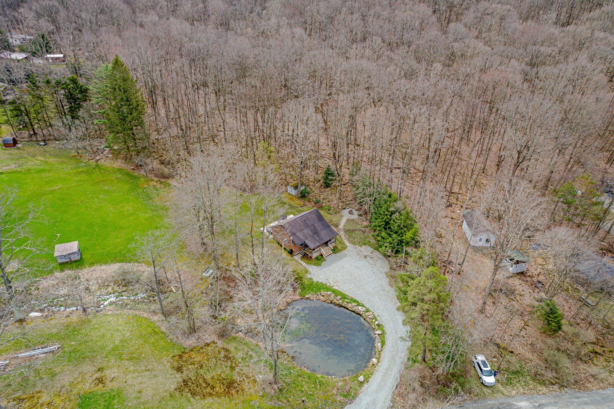 An aerial view of a rural property with a house, a pond, and a driveway.