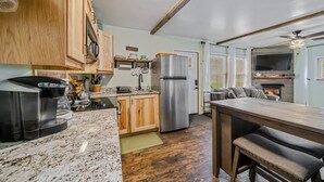 A kitchen with wooden cabinets, a stainless steel refrigerator, a coffee machine, and a dining area with a bench. - Cabin w/ Hot Tub on Small Pond (Rockwood)